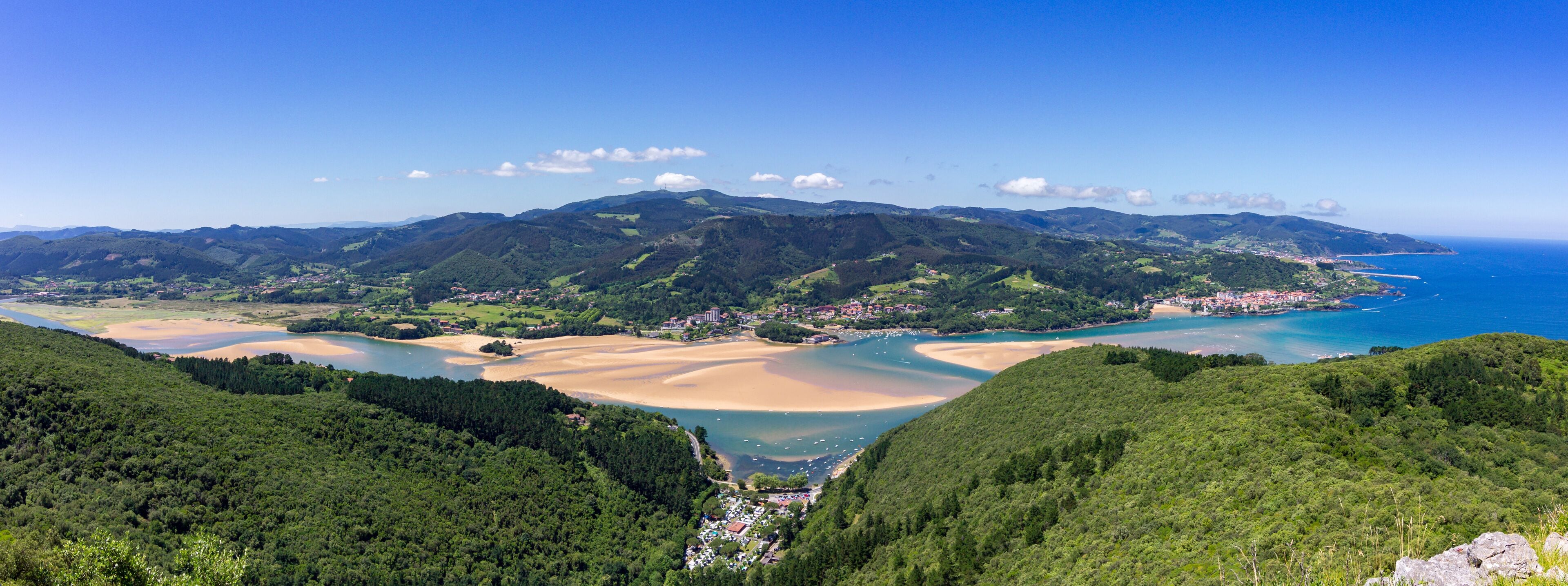 Paisagem costeira com uma baía, praias arenosas e colinas arborizadas.