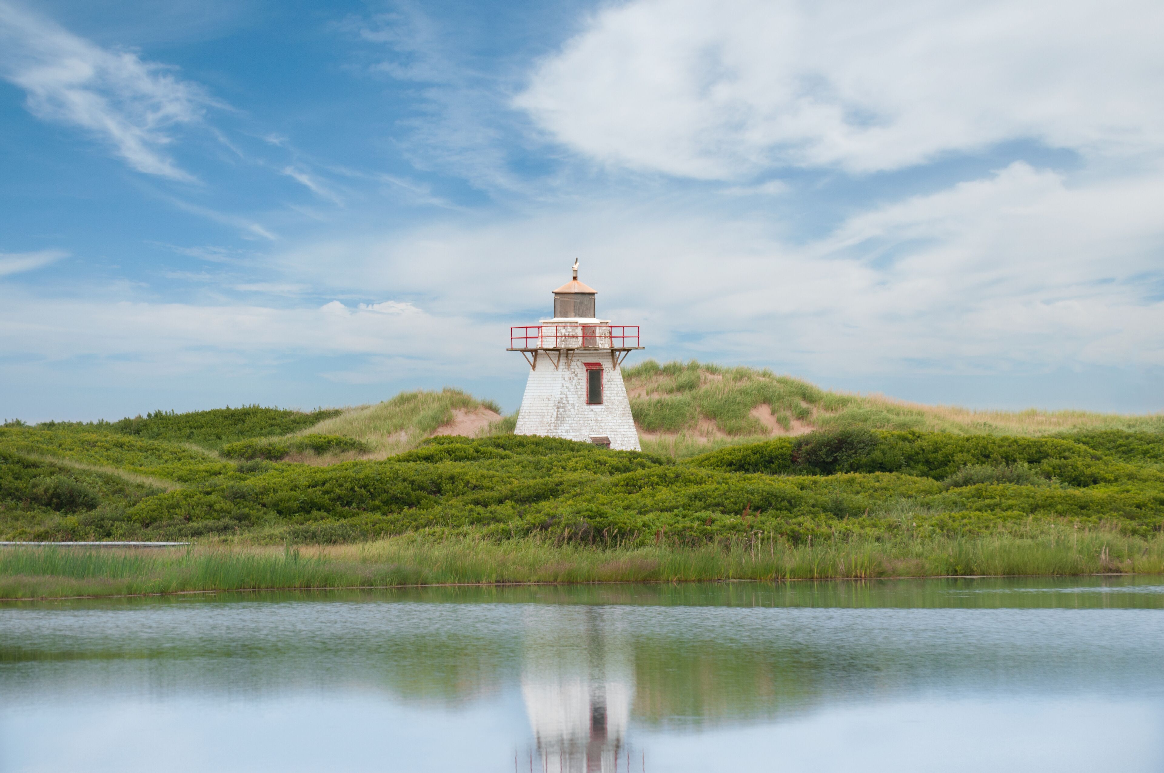 Close-up view of the lighthouse in St. Peter Harbour, Prince Edward Island, Canada, standing on sand dunes covered with green grass, reflecting on the water.