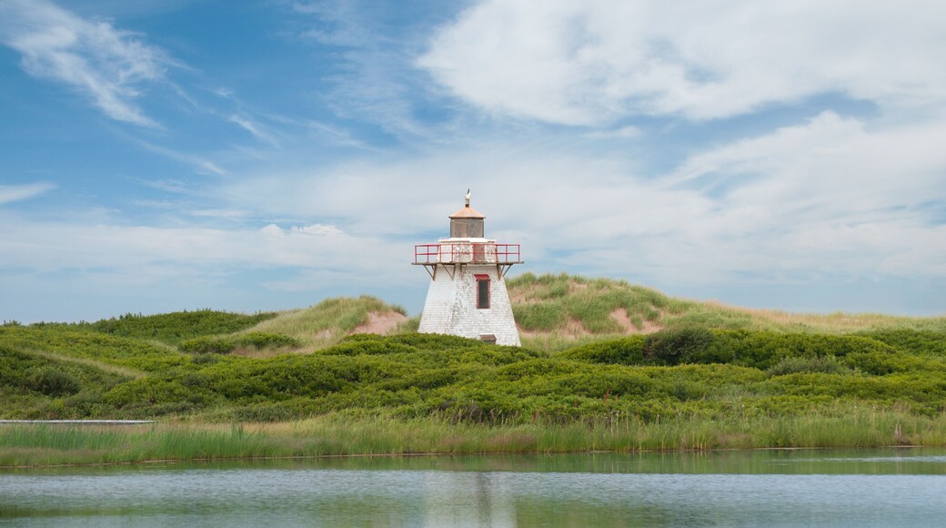 Close-up view of the lighthouse in St. Peter Harbour, Prince Edward Island, Canada, standing on sand dunes covered with green grass, reflecting on the water.