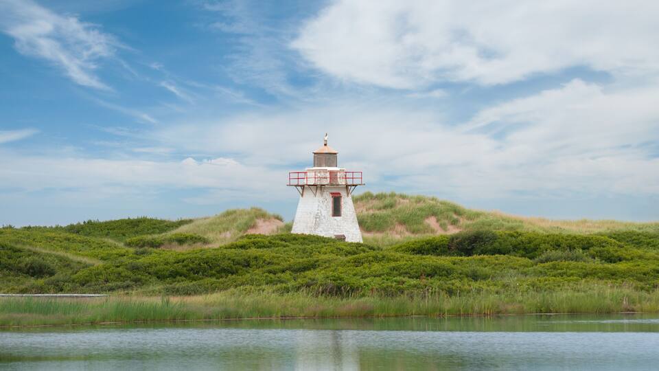 Close-up view of the lighthouse in St. Peter Harbour, Prince Edward Island, Canada, standing on sand dunes covered with green grass, reflecting on the water.