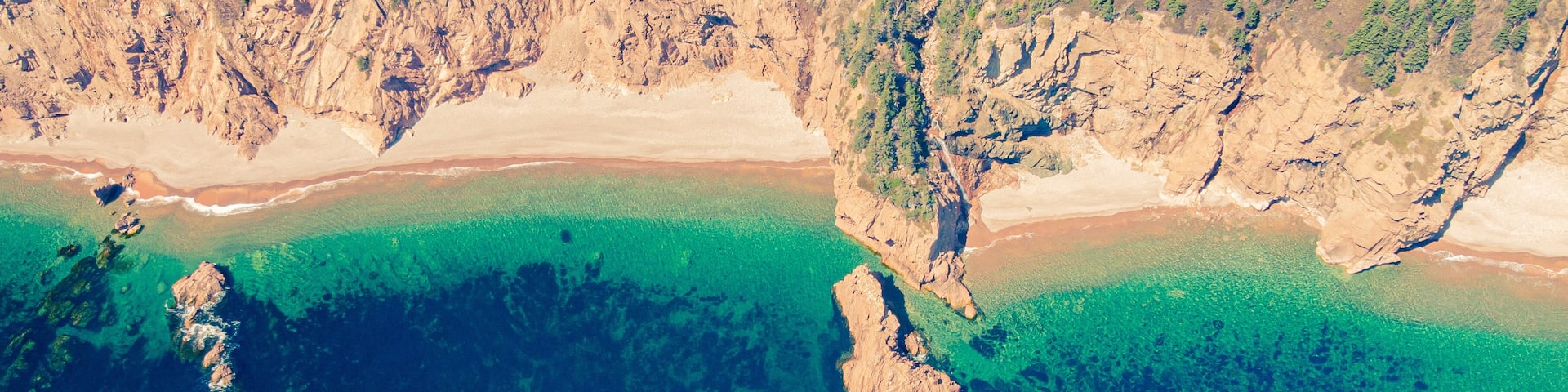 A coastal landscape with clear turquoise waters, rocky outcrops, and a sandy beach.