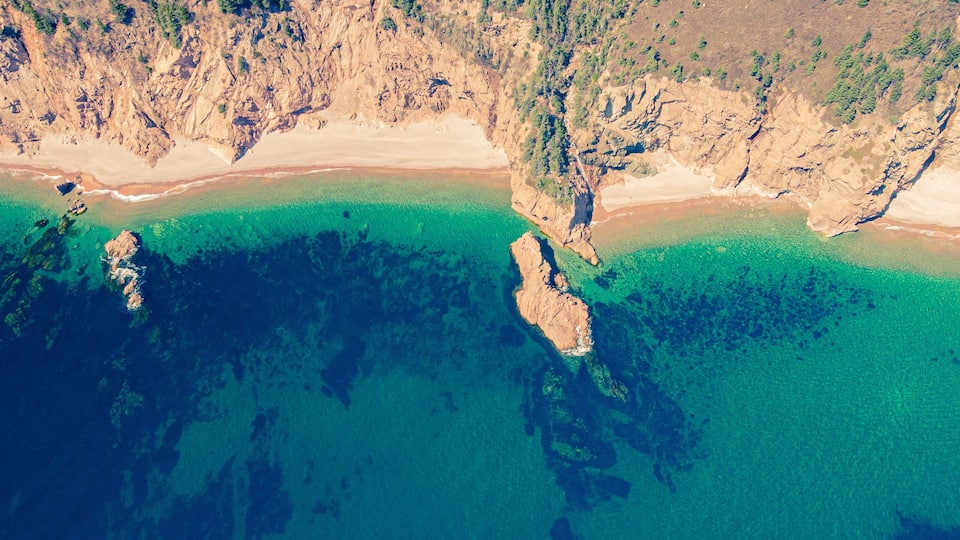 A coastal landscape with clear turquoise waters, rocky outcrops, and a sandy beach.