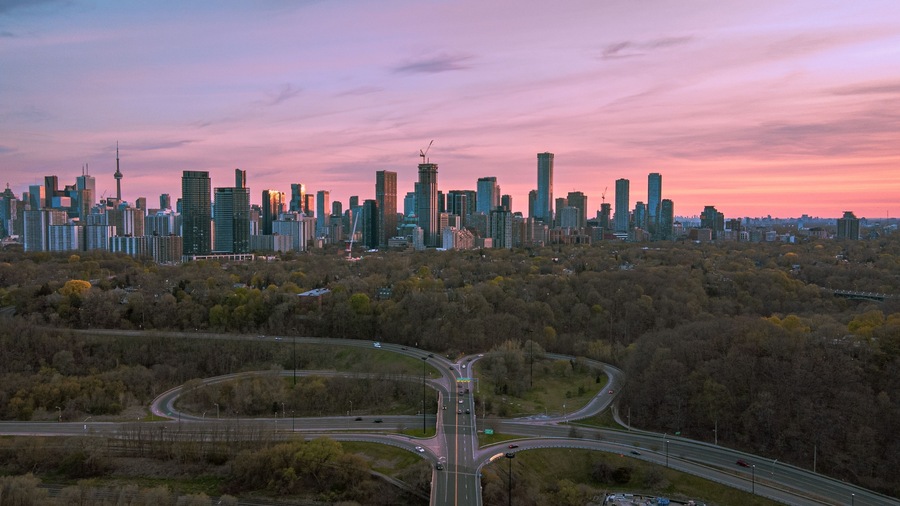 A city skyline with modern skyscrapers, a highway interchange, and a forested area.
