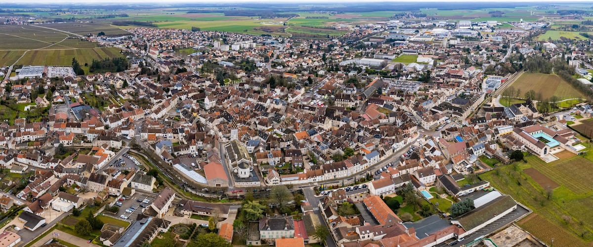 An aerial view of a densely populated town with a mix of residential and commercial buildings, surrounded by agricultural fields.