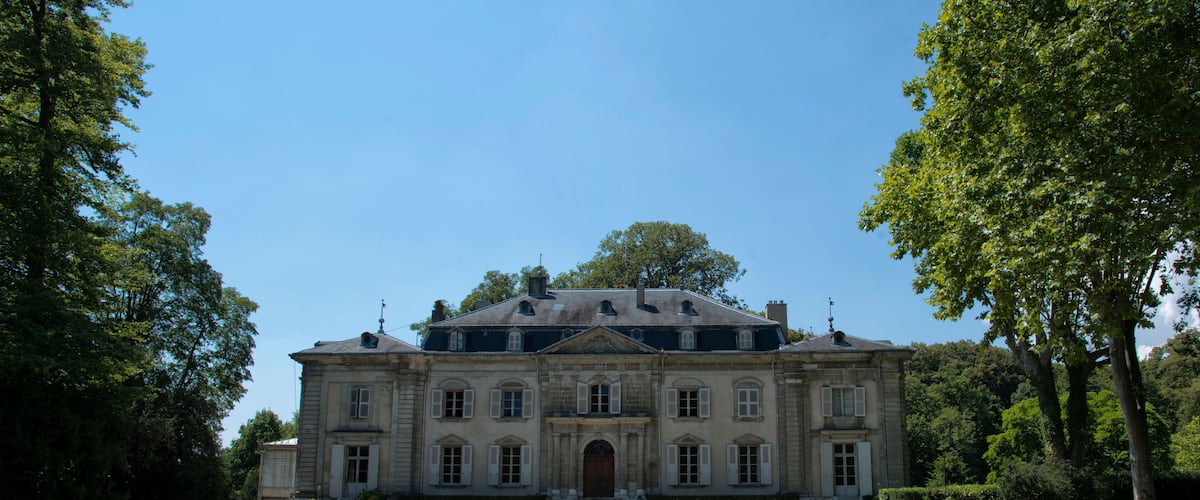 A large, historic building with a symmetrical facade, surrounded by lush greenery and trees.