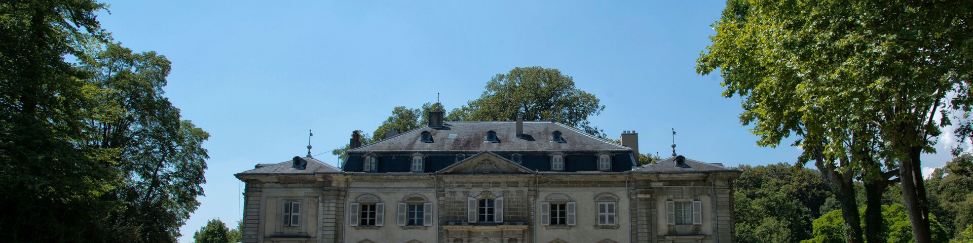 A large, historic building with a symmetrical facade, surrounded by lush greenery and trees.