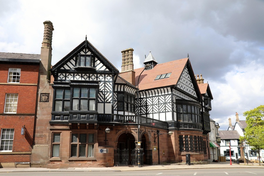 Un edificio de estilo Tudor con entramado de madera en blanco y negro, fachada de ladrillo y una chimenea destacada.