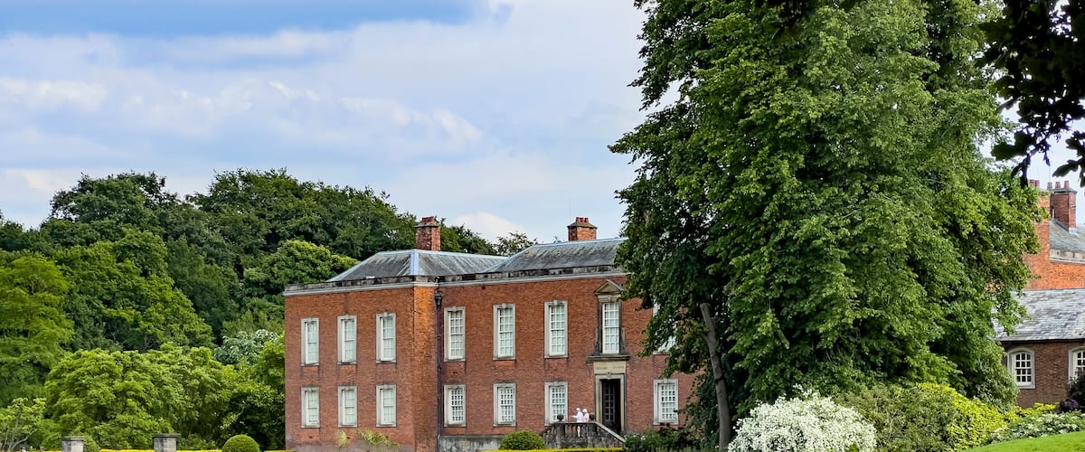 A large brick building with a pond in front, surrounded by trees and greenery.