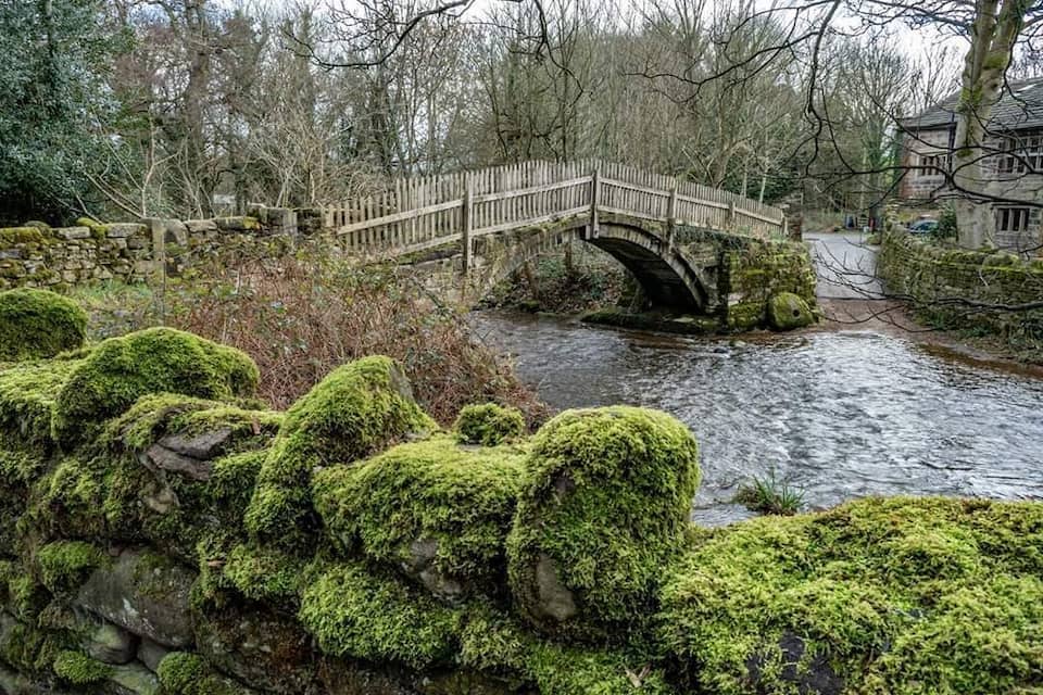 Een stenen brug over een rivier, omringd door begroeide rotsen en bomen.