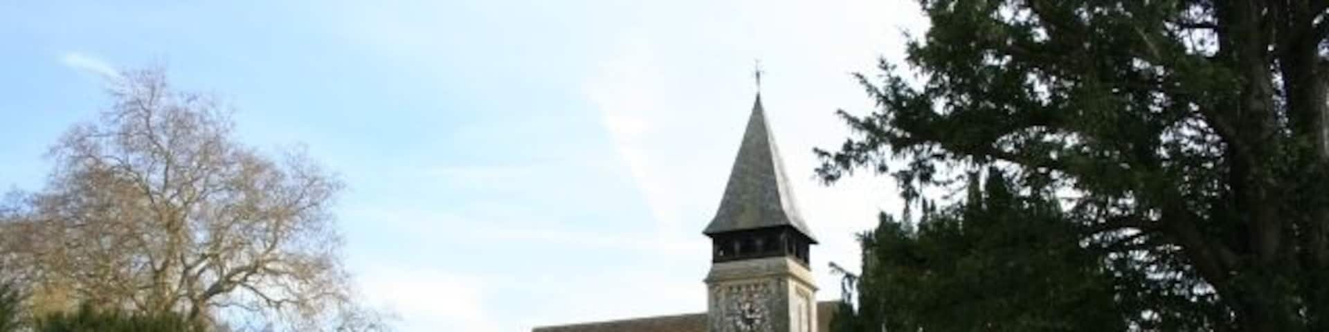 A church with a clock tower, surrounded by a grassy cemetery and trees.