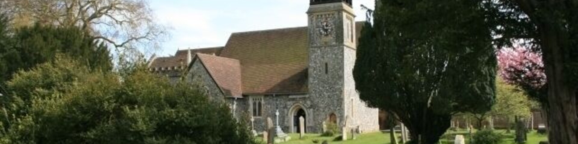 A church with a clock tower, surrounded by a grassy cemetery and trees.
