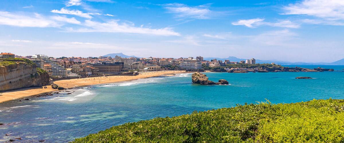 A coastal city with a sandy beach, rocky outcrops, and a mountainous backdrop.
