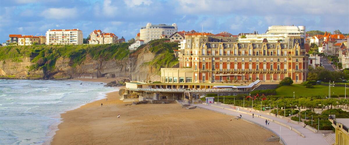 A coastal cityscape with a sandy beach, a promenade, and historic buildings.
