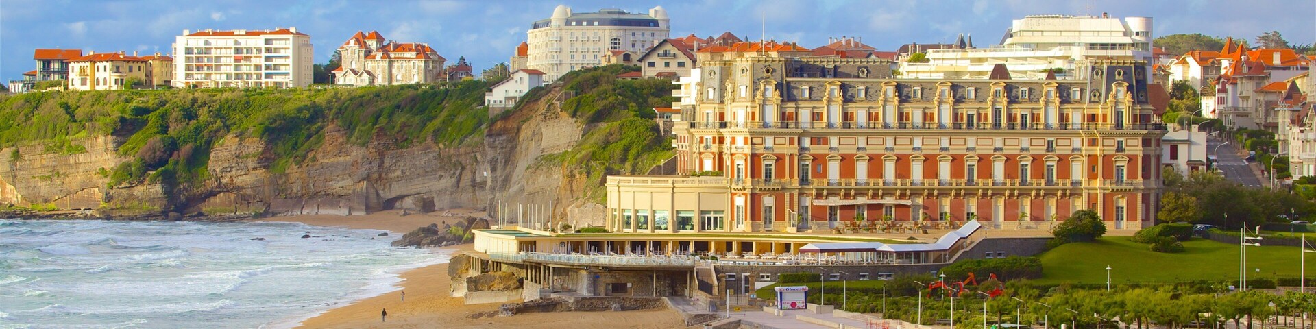 A coastal cityscape with a sandy beach, a promenade, and historic buildings.