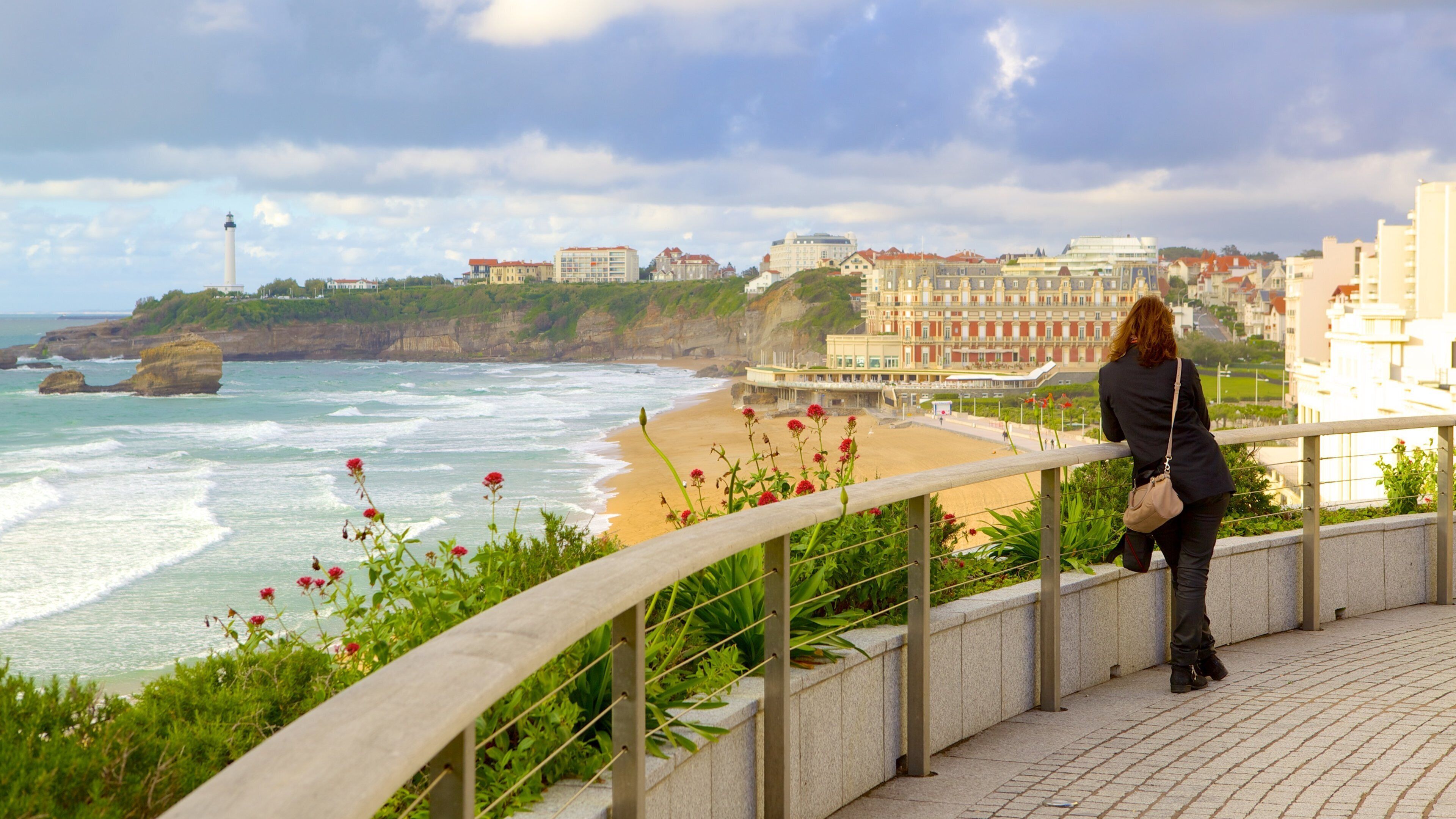 A coastal cityscape with a woman overlooking the beach, cliffs, and buildings.