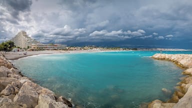 A coastal scene with a hotel, clear turquoise waters, rocky shoreline, and a cloudy sky.