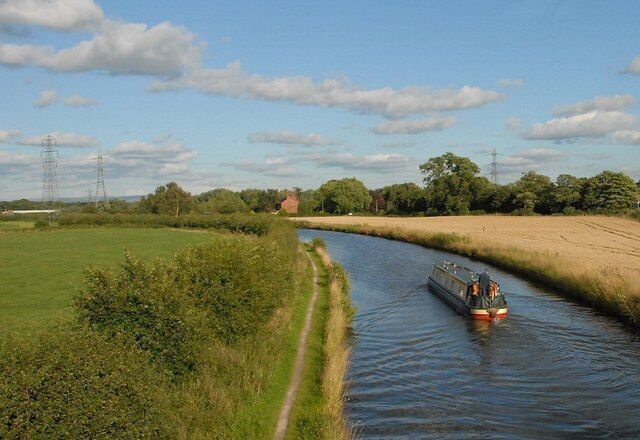 A narrow waterway with a boat, surrounded by green fields and trees under a partly cloudy sky.