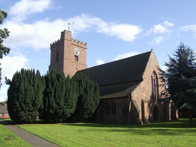 A church with a clock tower and a large tree in front.