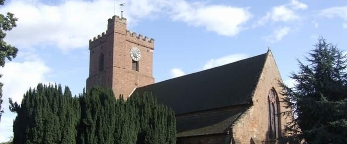 Una iglesia con una torre del reloj y un árbol grande en primer plano.