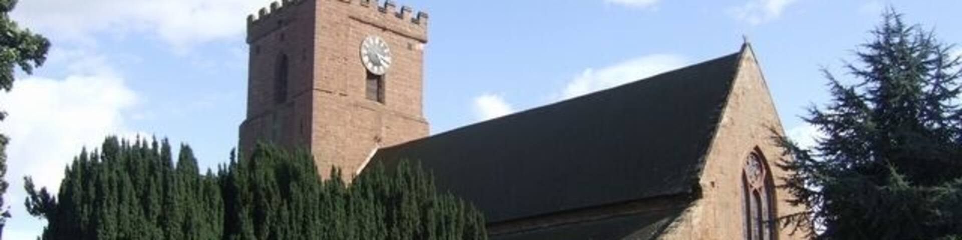 A church with a clock tower and a large tree in front.