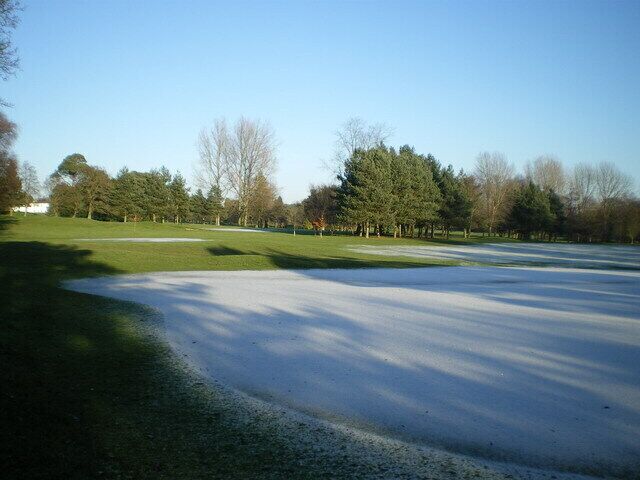 Un campo de golf con un putting green, árboles y un cielo despejado.