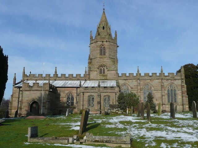 A historic church with a tall spire, arched windows, and a cemetery in front.