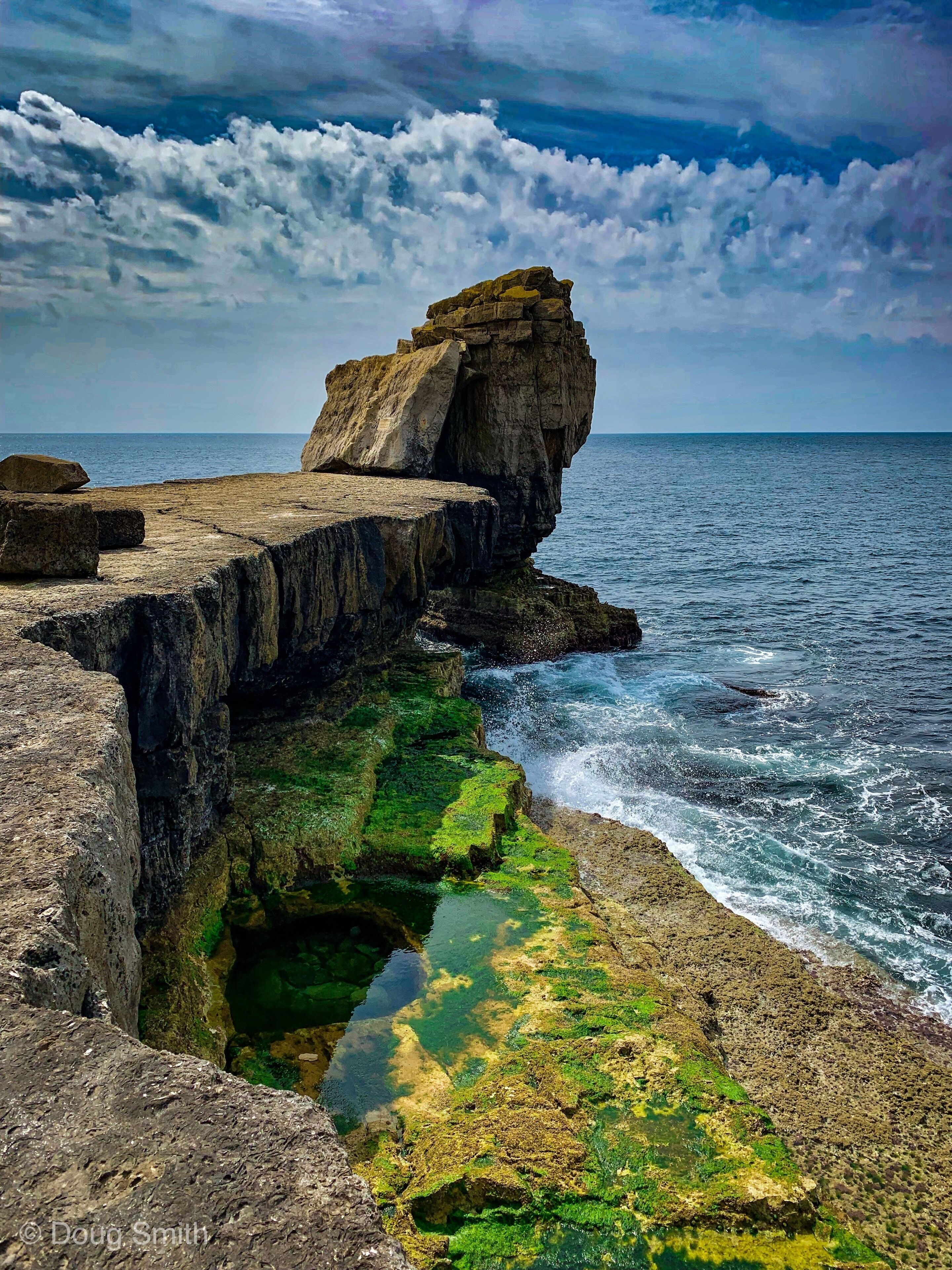 A rocky coastline with a prominent rock formation and green algae-covered rocks.