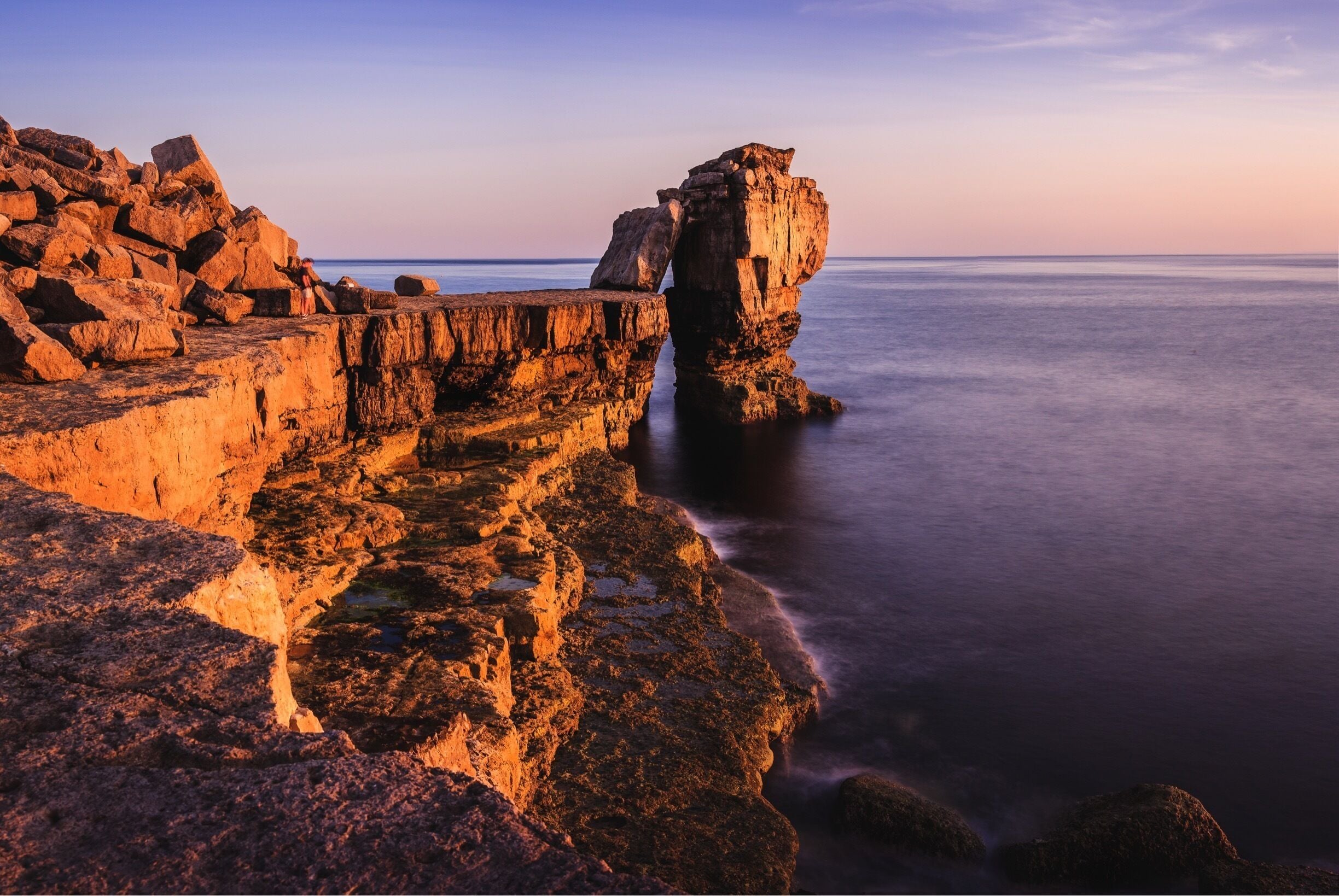 A rocky coastline with a prominent rock formation at sunset.