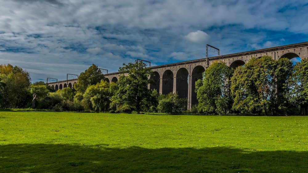 Un viaduc en pierre, doté de plusieurs arches, entouré d’une végétation luxuriante et d’arbres.