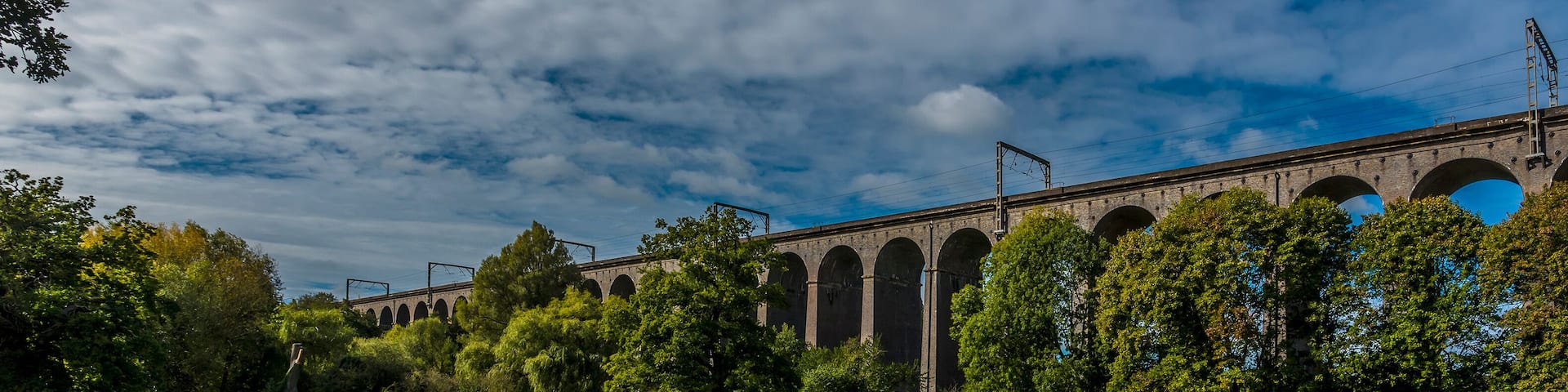 A stone viaduct with multiple arches, surrounded by lush green grass and trees.