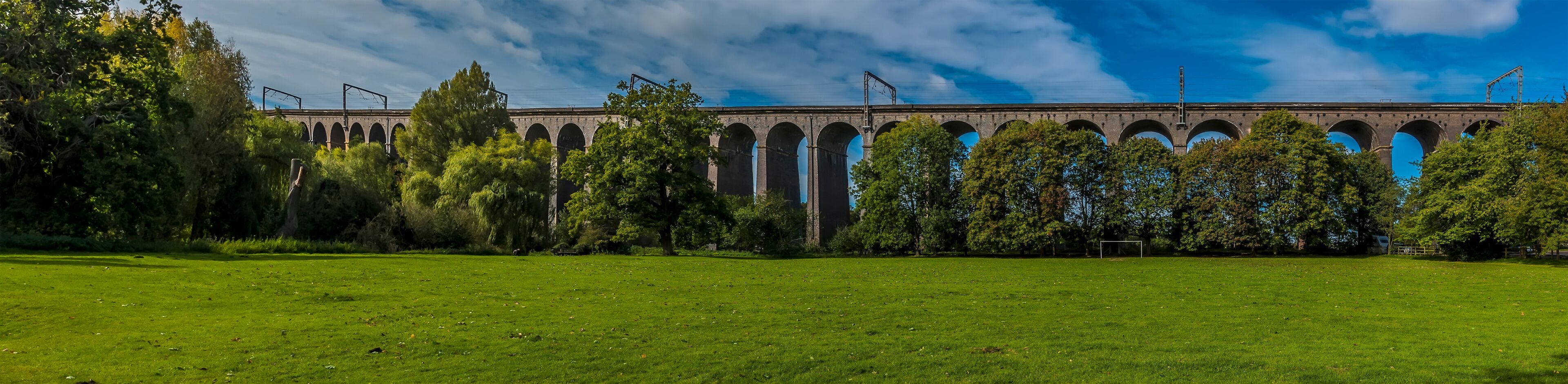 A large green field with a historic stone bridge in the background.
