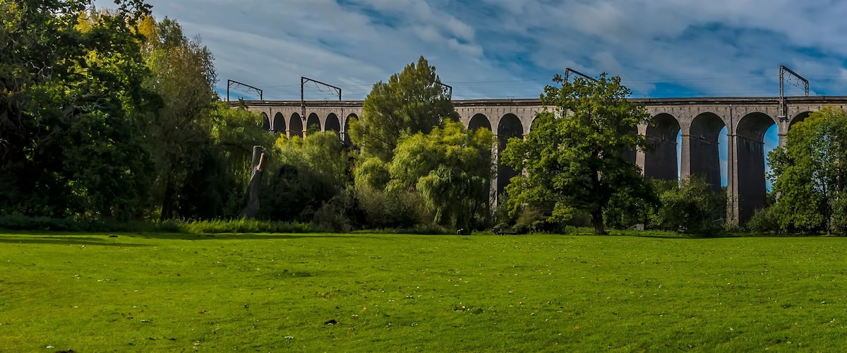 A large green field with a historic stone bridge in the background.