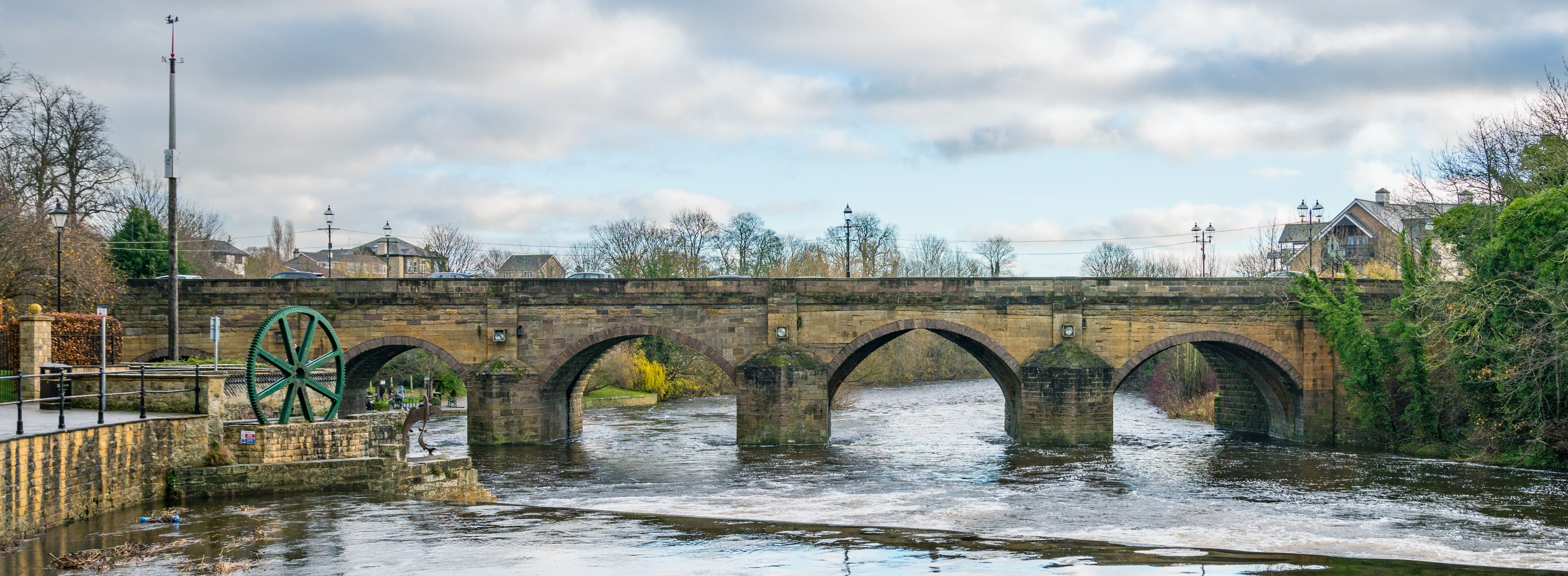 A stone bridge with multiple arches over a river, surrounded by trees and buildings.