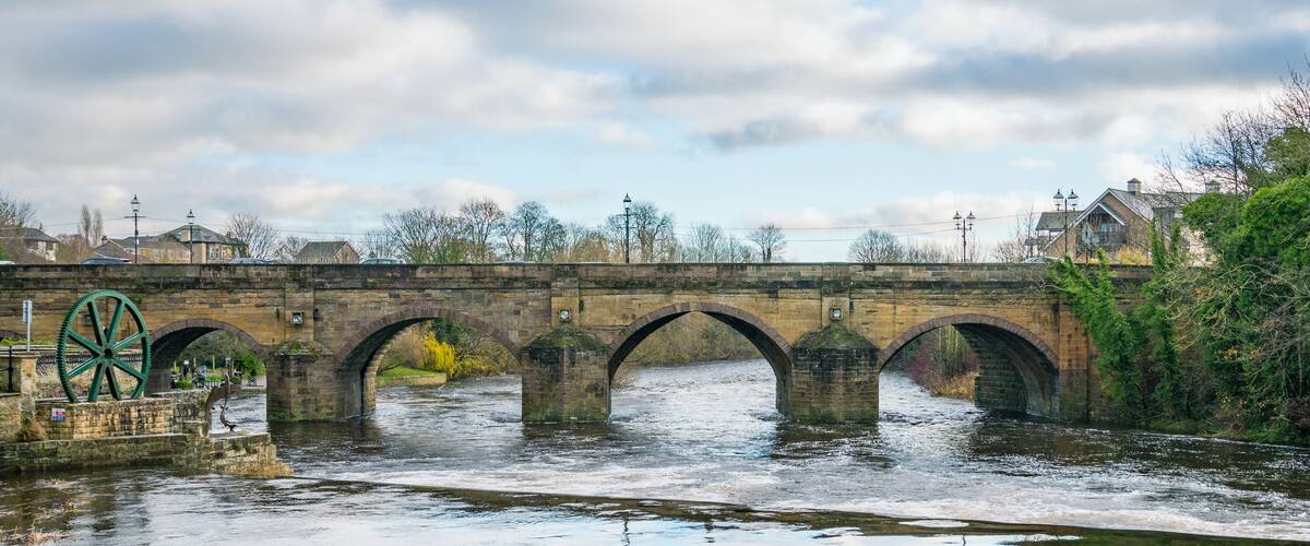 A stone bridge with multiple arches over a river, surrounded by trees and buildings.