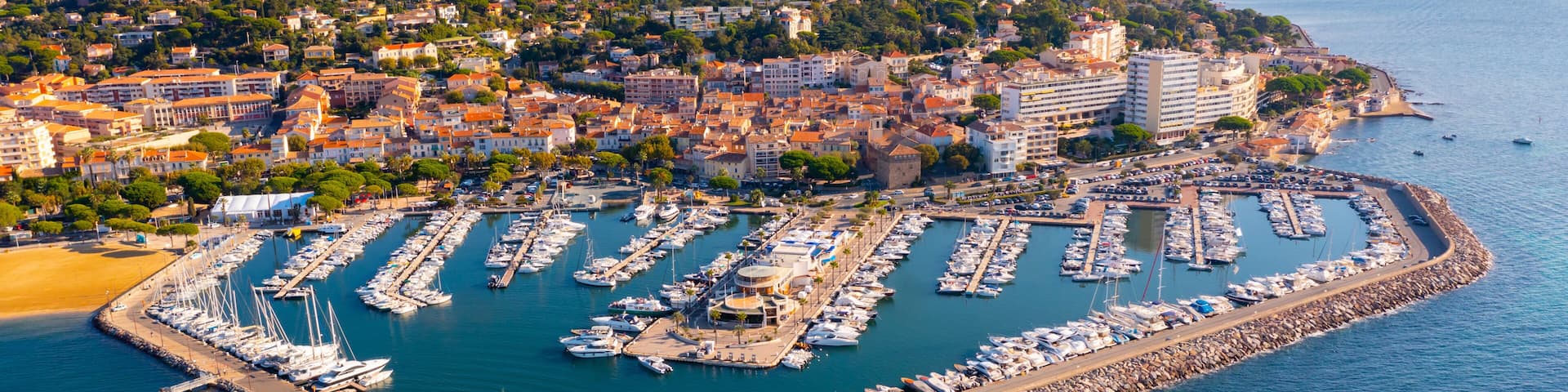 Summer aerial view of French coastal town of Sainte-Maxime on Mediterranean coast overlooking marina with moored pleasure yachts and residential houses on green hills