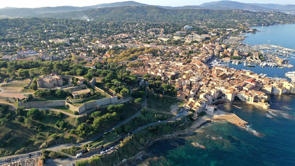 An aerial view of a coastal town with a historic fort, dense residential area, and a marina.