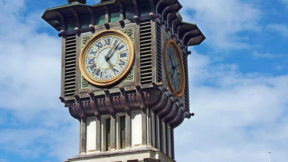 A clock tower with Roman numerals and a spire against a blue sky.