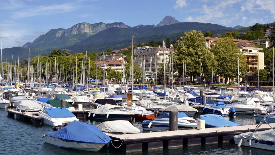 A marina with numerous boats docked, surrounded by mountains and residential buildings.