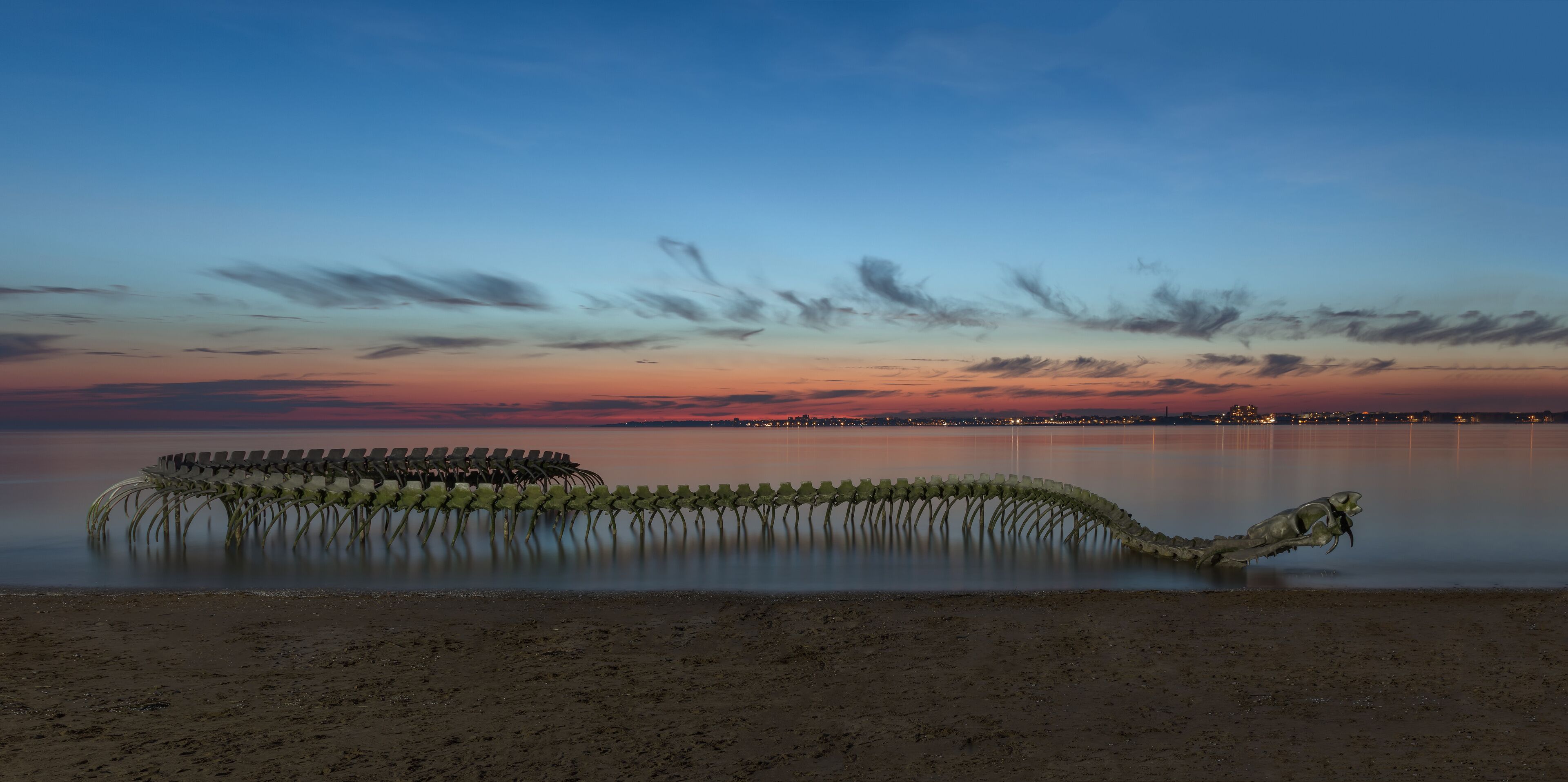A sunset over a calm lake with a unique sculpture of chairs in the water.