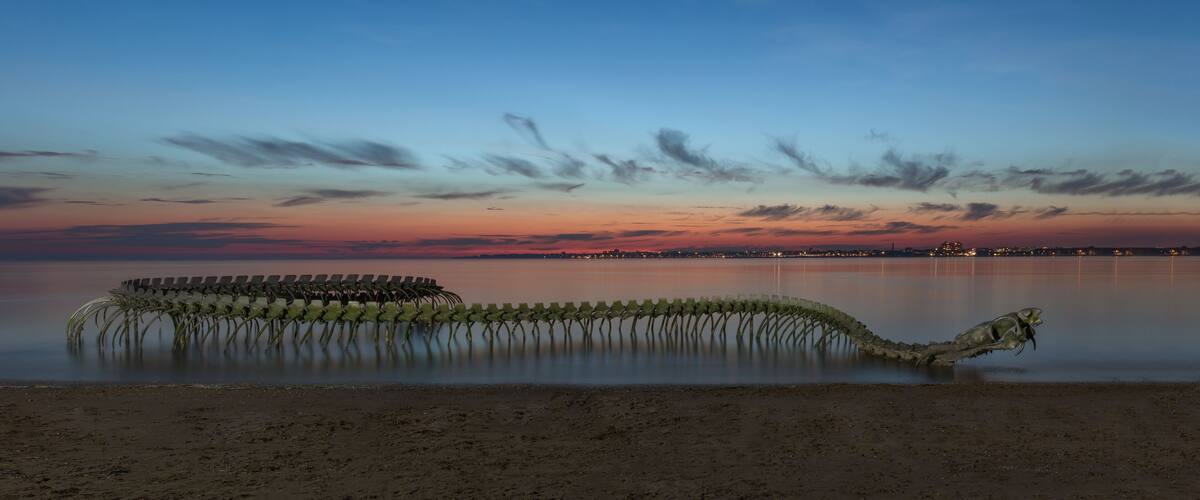 A sunset over a calm lake with a unique sculpture of chairs in the water.
