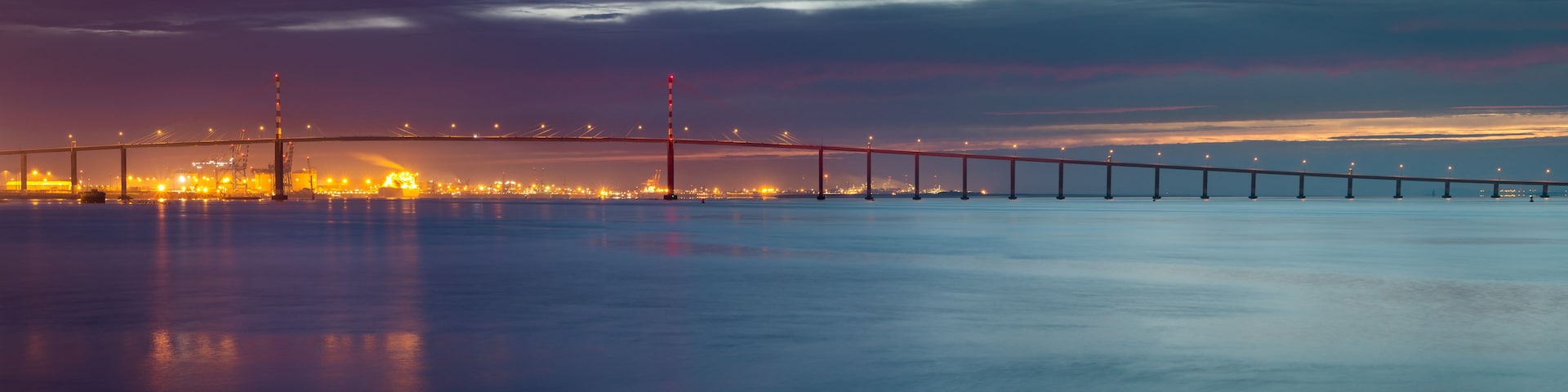 A bridge spanning a body of water with city lights in the background.
