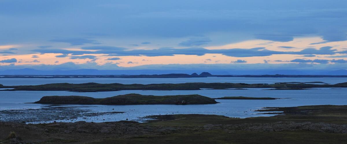 A coastal landscape with multiple small islands and a distant mountain range under a twilight sky.