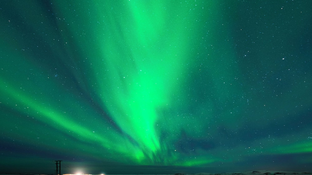 The Northern Lights over a snowy landscape with a road and a power line.