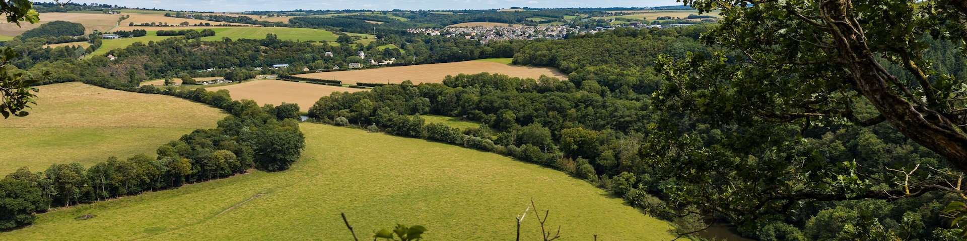 A river winding through a lush valley with rolling green fields and dense forests.