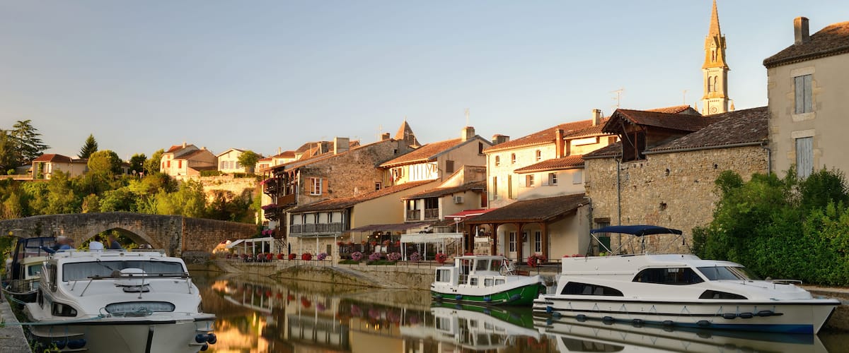 A canal with boats docked, historic buildings, and a church spire.