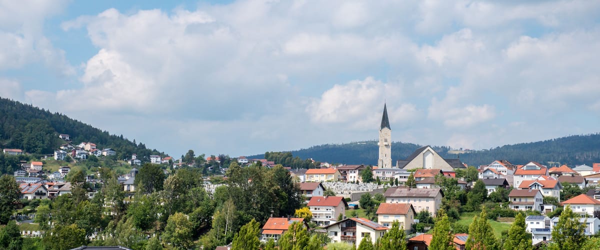 A town with a prominent church steeple, surrounded by residential houses and lush greenery.