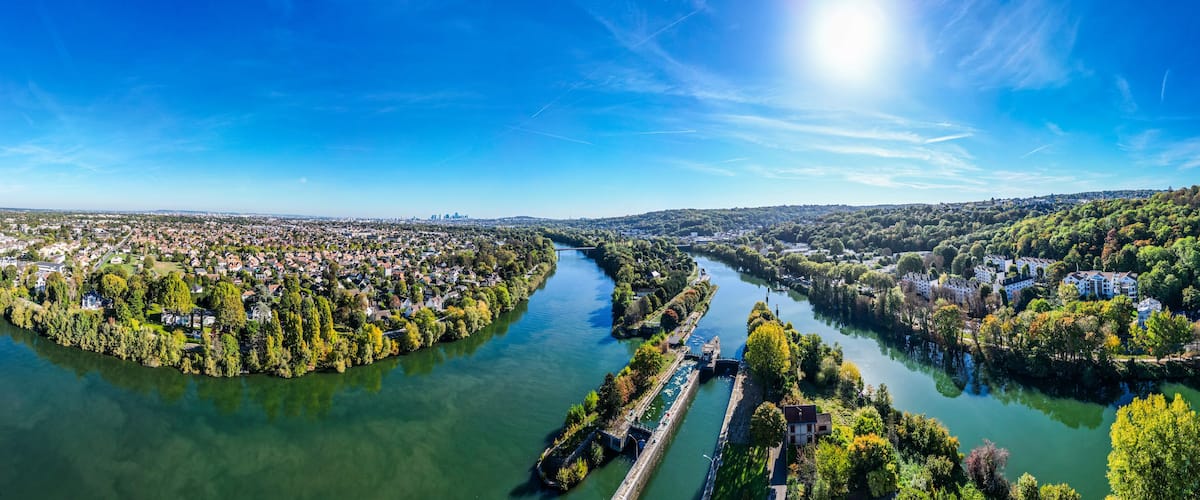 A river winding through a densely populated urban area with surrounding greenery and a clear blue sky.