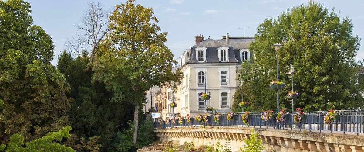 A stone bridge with hanging flower baskets, a river, and trees.
