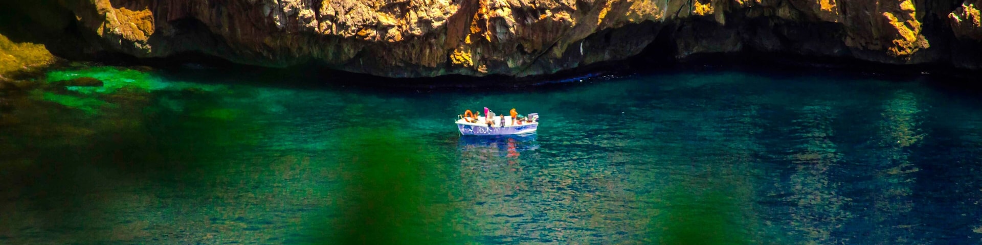 Un barco en un mar turquesa cristalino con acantilados rocosos al fondo.