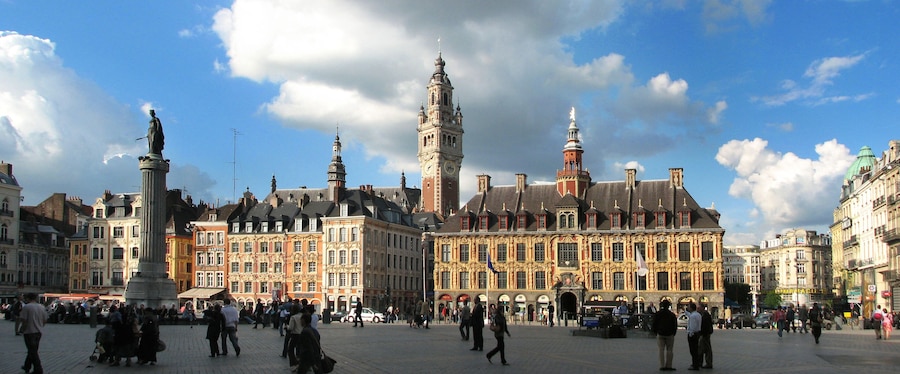 A historic square with a prominent clock tower, a statue, and ornate buildings.